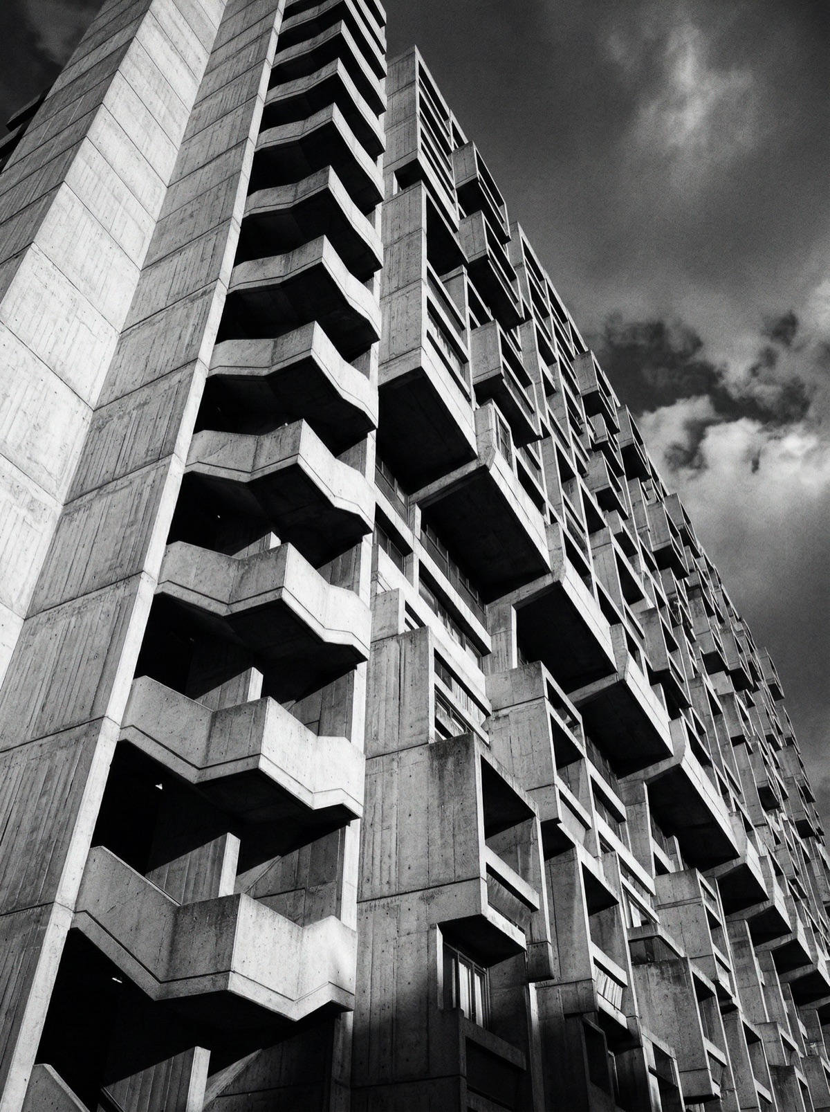 Monochromatic black and white photograph of Brutalist architecture featuring dramatic shadows, clean lines, and repetitive concrete patterns